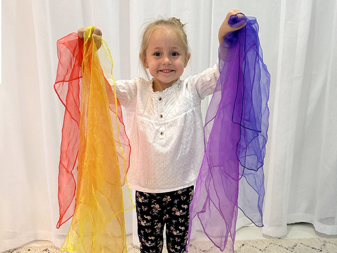 Young children playing with colorful rainbow play scarves, tossing and catching them indoors
