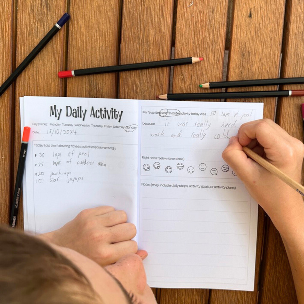 Person filling out a daily activity log with pencils on a wooden surface